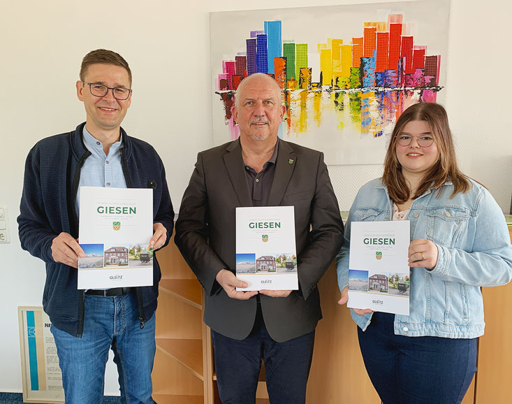 Bürgermeister Frank Jürges (Mitte) präsentiert zusammen mit dem Technischen Leiter Oliver Kroll und Mediengestalterin Daria-Sue Göhr die gemeinsam neu aufgelegte Broschüre der Gemeinde Giesen.